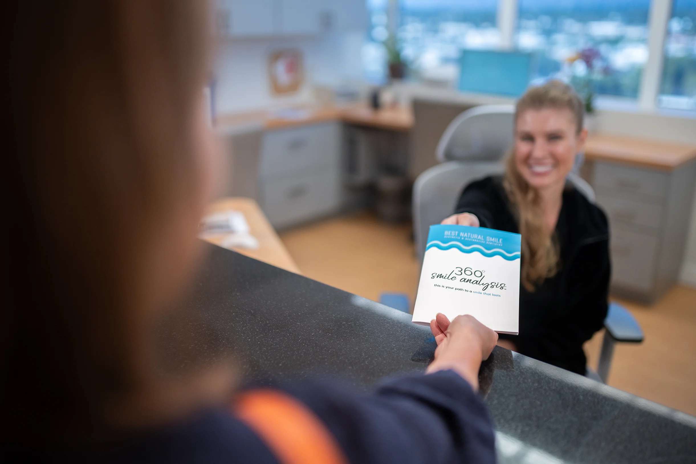 Front desk handing patient a Best Natural Smile 360° smile analysis brochure.